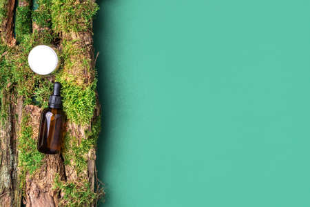 Amber glass cosmetic bottle on green background, natural moss over branches, bark. Skin care, organic body treatment, spa concept. Vegan eco friendly cosmetology product. Organic cosmetics.の写真素材