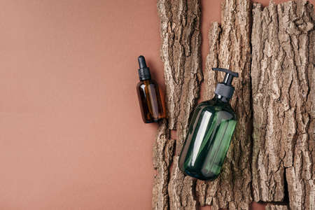 Green glass bottle of shampoo, soap, conditioner on beige background with natural bark, wood. Top view, copy space. Blank label for mock-up. Skin care, organic body treatment, spa conceptの写真素材