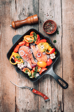 Raw uncooked salmon fish with vegetables, herbs, spices in iron grilling pan over wooden background. Top view, copy space. Healthy food. Dinner cooking ingredients.の写真素材