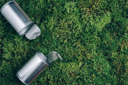 Open tin can on green moss background. Top view. Copy space. Aluminium cans after picnic in forest. Environmental pollution problem. Garbage, waste collection and sorting, trash outdoorsの写真素材
