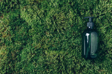Green glass bottle of shampoo, soap, conditioner on green moss background. Biophilic design. Top...