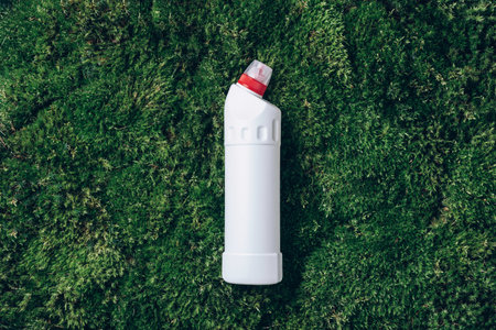 White plastic bottle of cleaning product, household chemicals or liquid laundry detergent on green...