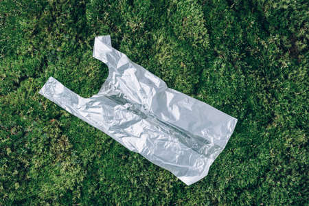 Pollution problem concept. Disposable plastic bag on green moss, grass background. Top view. Copy space. Environmental pollution problem. Garbage, waste collection and sorting, trash outdoorsの写真素材