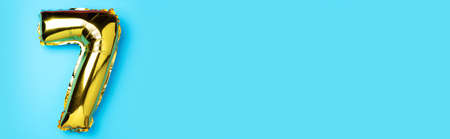 Creative layout. Golden foil balloon number and digit seven 7. Birthday greeting card. Anniversary concept. Top view. Copy space. Stylish gold numeral over blue background. Numerical digit.の写真素材