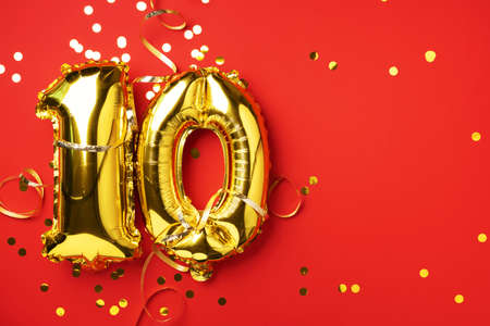 Gold foil balloon number, digit ten. Birthday greeting card with inscription 10. Anniversary celebration event. Banner. Golden numeral, red background. Numerical digit, bright shiny glitterの写真素材