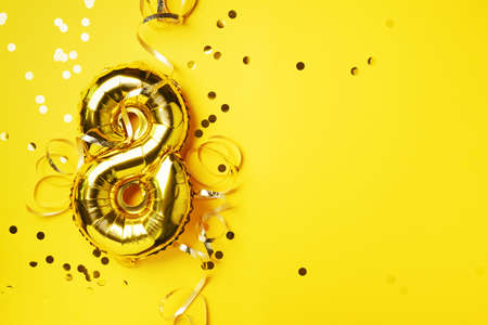 8 March. Happy Womens Day. Gold foil balloon number and digit eight 8. Birthday greeting card. Anniversary celebration event. Banner. Golden numeral, yellow background. Numerical digit.の写真素材
