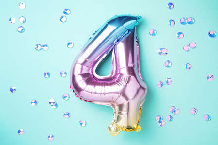 Creative layout. Rainbow foil balloon number and digit four 4. Birthday greeting card. Anniversary concept. Top view. Copy space. Stylish colored numeral over blue background. Numerical digit.の写真素材