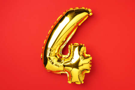 Creative layout. Golden foil balloon number and digit four 4. Birthday greeting card. Anniversary concept. Top view. Copy space. Stylish gold numeral over red background. Numerical digit.の写真素材