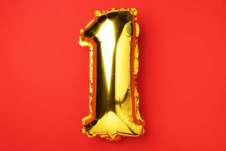 Creative layout. Golden foil balloon number and digit one 1. Birthday greeting card. Anniversary concept. Top view. Copy space. Stylish gold numeral over red background. Numerical digit.の写真素材