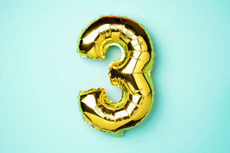 Creative layout. Golden foil balloon number and digit three 3. Birthday greeting card. Anniversary concept. Top view. Copy space. Stylish gold numeral over blue background. Numerical digit.の写真素材