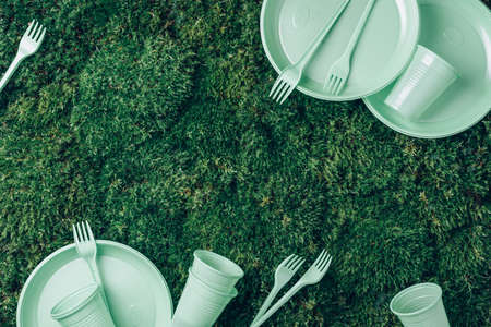 Recycling plastic and ecology. Disposable plastic tableware - plates, forks, spoons, knives. Top view. Copy space. Environmental pollution. Pastel plastic waste on green grass, moss backgroundの写真素材