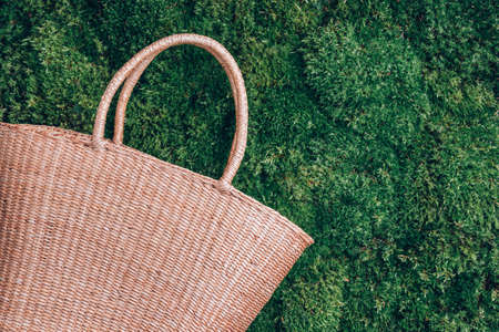 Straw mesh bag on green grass moss background. Summer picnic in forest. Top view. Copy space. Outdoor recreation. Digital Detox. Unplugging, mindfulnessの写真素材