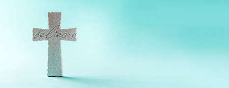 Stone cross with inscription Believe on grey background, Copy space. Christian backdrop. Biblical faith, gospel, salvation concept. Bannerの写真素材