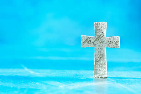 Stone cross with inscription Believe on blue background, Copy space. Christian backdrop. Biblical faith, gospel, salvation concept. Bannerの写真素材
