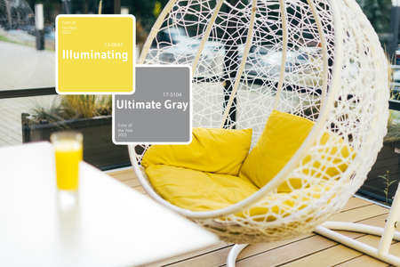 Hanging wicker chair with yellow cushions in minimalistic style outdoor interior. Demonstrating trendy Color of the Year 2021. Illuminating Yellow and Ultimate Gray. Duotone. Depression treatmentの写真素材