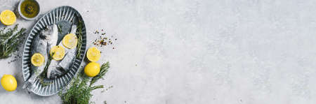 Uncooked dorado or sea bream fish with lemon, herbs, oil, vegetables and spices on concrete...
