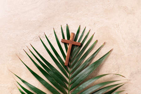 Palm Sunday concept. Wooden cross over palm leaves. Reminder of Jesus sacrifice and Christ resurrection. Easter passover. Eucharist concept. Christianity symbol and faithの写真素材