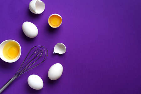 Eggs in white bowl with whisk on violet background. Baking frameの写真素材