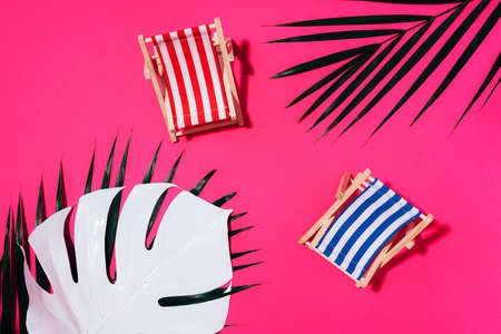 Two deck chairs with hard shadow, monstera and palm leaves on pink paper background. Flat lay and copy space. Summer travel vacation concept. Minimal compositionの写真素材