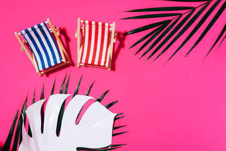 Deck chairs with hard shadow, monstera and palm leaves on pink paper background. Flat lay and copy space. Summer travel vacation concept. Minimal composition.の写真素材
