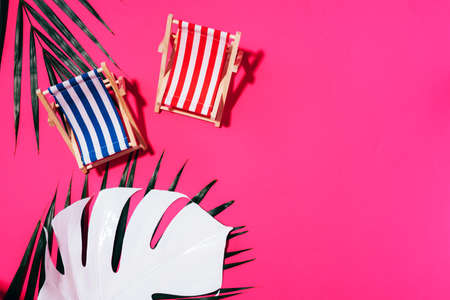 Flat lay of beach deck chairs, monstera and palm leaves on pink background with copy space. Summer and travel concept. Creative bannerの写真素材