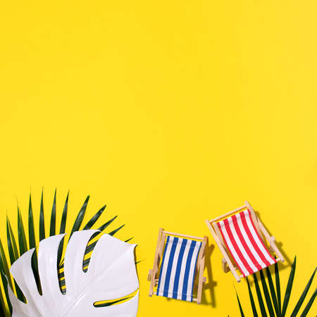 Deck chairs with hard shadow, monstera and palm leaves on yellow paper background. Flat lay and copy space. Summer travel vacation concept. Minimal compositionの写真素材