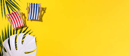 Deck chairs with hard shadow, monstera and palm leaves on yellow paper background. Flat lay and copy space. Summer travel vacation concept. Minimal compositionの写真素材