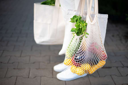 Girl holding mesh shopping bag and cotton shopper with vegetables without plastic bags at farmers market. Zero waste, plastic free concept. Sustainable lifestyle. Banner.の写真素材