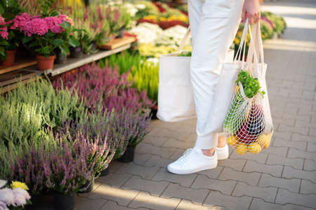 Zero waste concept with copy space. Woman holding cotton shopper and reusable mesh shopping bags with vegetables, products. Eco friendly mesh shopper. Zero waste, plastic free concept.の写真素材