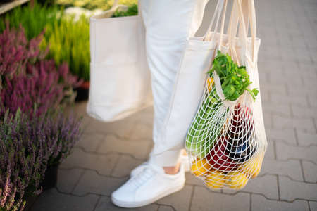 Girl holding mesh shopping bag and cotton shopper with vegetables without plastic bags at farmers market. Zero waste, plastic free concept. Sustainable lifestyle. Banner.の写真素材