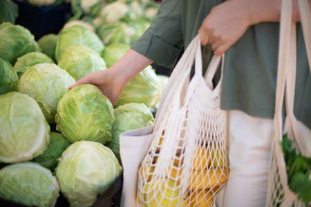Zero waste, plastic free concept. Sustainable lifestyle. Woman chooses fruits and vegetables at farmers market. Reusable cotton and mesh eco bags for shopping.の写真素材