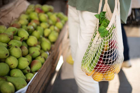 Woman chooses fruits and vegetables at farmers market. Zero waste, plastic free concept. Sustainable lifestyle. Reusable cotton and mesh eco bags for shopping.の写真素材