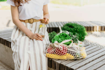 Girl holding mesh shopping bag and cotton shopper with vegetables without plastic bags, wooden background. Zero waste, plastic free concept. Sustainable lifestyle. Banner.の写真素材
