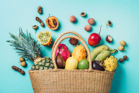Exotic fruits in straw summer bag. Tropical pineapple, banana, pitahaya, kiwano, african horned melon, tamarillo fruit, granadilla, salak, snake fruit, maracuya, rambutan, lychee, longan, tamarind, mangosteen on blue background. Top view. Copy space. Sustainable lifestyle. Zero waste, plastic free conceptの写真素材
