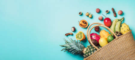 Exotic fruits in straw summer bag on blue background. Top view. Copy space. Tropical fruits flat lay. Zero waste, plastic free concept. Travel and holiday concept. Vegan, vegetarian healthy diet. Bannerの写真素材
