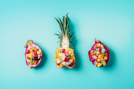Exotic fruit salad served in half of dragon fruit and pineapple fruit on blue background. Copy...