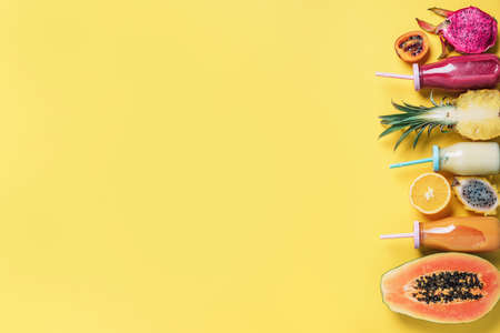 Detox summer drink. Vegan, vegetarian, fructorian diet. Fresh smoothie and juicy fruits - papaya, orange, pineapple, dragon fruit, pitahaya, tamarillo fruit over yellow background. Top view, flat lay, copy space.の写真素材