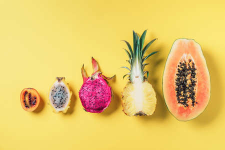Creative layout made of exotic fruits - papaya, pineapple, dragon fruit, pitahaya, tamarillo fruit on yellow background. Flat lay. Top view. Copy space. Summer food, tropical fruits concept. Vegan, fructorian diet.の写真素材