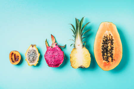 Creative layout made of exotic fruits - papaya, pineapple, dragon fruit, pitahaya, tamarillo fruit on blue background. Flat lay. Top view. Copy space. Summer food, tropical fruits concept. Vegan, fructorian diet.の写真素材