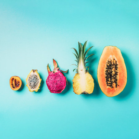 Creative layout made of exotic fruits - papaya, pineapple, dragon fruit, pitahaya, tamarillo fruit on blue background. Flat lay. Top view. Copy space. Summer food, tropical fruits concept. Vegan, fructorian diet.の写真素材