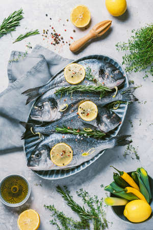 Fresh uncooked dorado or sea bream fish with lemon, herbs, oil, vegetables and spices on concrete...