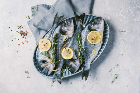 Uncooked dorado or sea bream fish with lemon, herbs, oil, vegetables and spices on concrete background. Top view. Healthy food concept. Copy space. Food patternの写真素材
