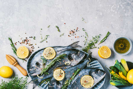 Cooking dorado or sea bream fish with lemon, herbs, oil, vegetables and spices on concrete background. Seafood concept. Top view. Healthy food concept. Copy space. Food patternの写真素材