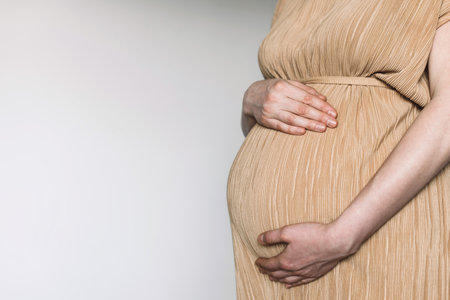 Pregnancy, maternity, preparation, baby expectation concept. 40 weeks of pregnancy. Pregnant woman in beige dress touching belly, preparing go to maternity hospital for childbirth. White backgroundの写真素材