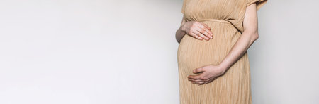 Pregnant woman in beige dress touching belly, preparing go to maternity hospital for childbirth. Pregnancy, maternity, preparation, baby expectation concept. 40 weeks of pregnancy. White backgroundの写真素材