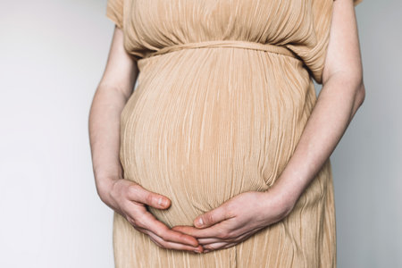 Pregnant woman in beige dress touching belly, preparing go to maternity hospital for childbirth. Pregnancy, maternity, preparation, baby expectation concept. 40 weeks of pregnancy. White backgroundの写真素材