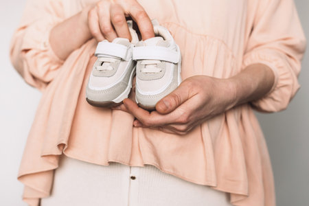Pregnant woman in pink dress holding small shoes for unborn baby on belly, preparing go to maternity hospital for childbirth. Pregnancy, maternity, preparation, baby expectation concept. Copy spaceの写真素材