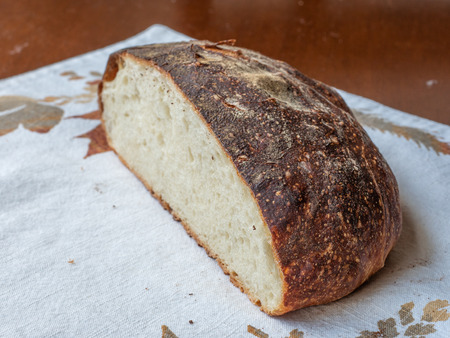 Freshly baked artisan loaf of bread cut to show crumb texture and crusty exterior, resting on a fall...