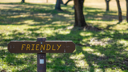 Brown wooden sign in grassy field with friendly written on itの写真素材