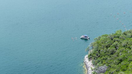 Pontoon boat anchored near the shoreline of a lake, with occupants swimming